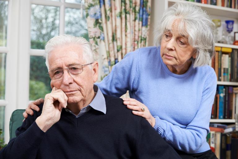 En ældre trist mand og en kvinde, der lægger hænderne på hans skuldre