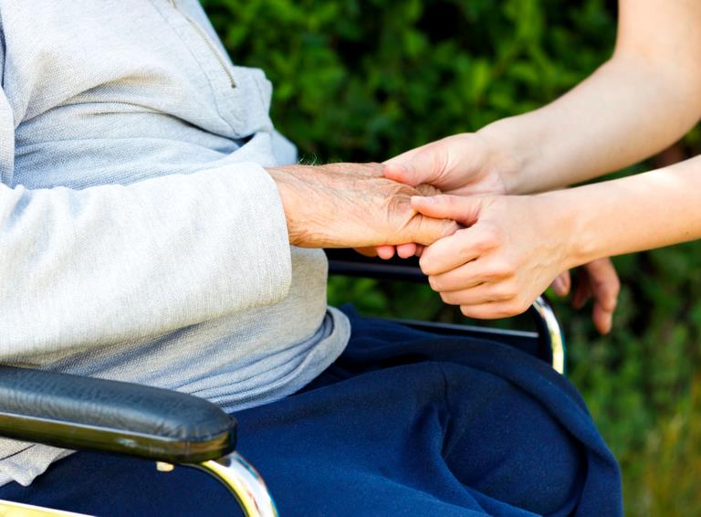 En ældre person i kørestol bliver holdt i hånden af en yngre person