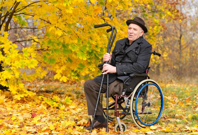 En mand i kørestol med krykker i hånden i en skov med efterårsfarver