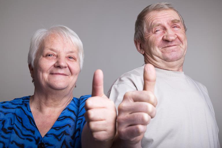 Et smilende par seniorer med tommelfingrene opad